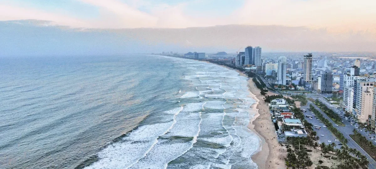 Aerial view of the Da Nang beachfront with surf, sand and hotel towers along the coast road