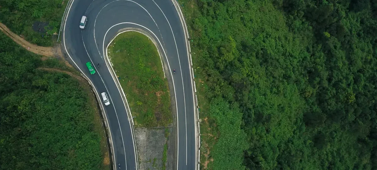 Aerial view of cars rounding a hairpin bend on the forested Hai Van Pass road north of Da Nang