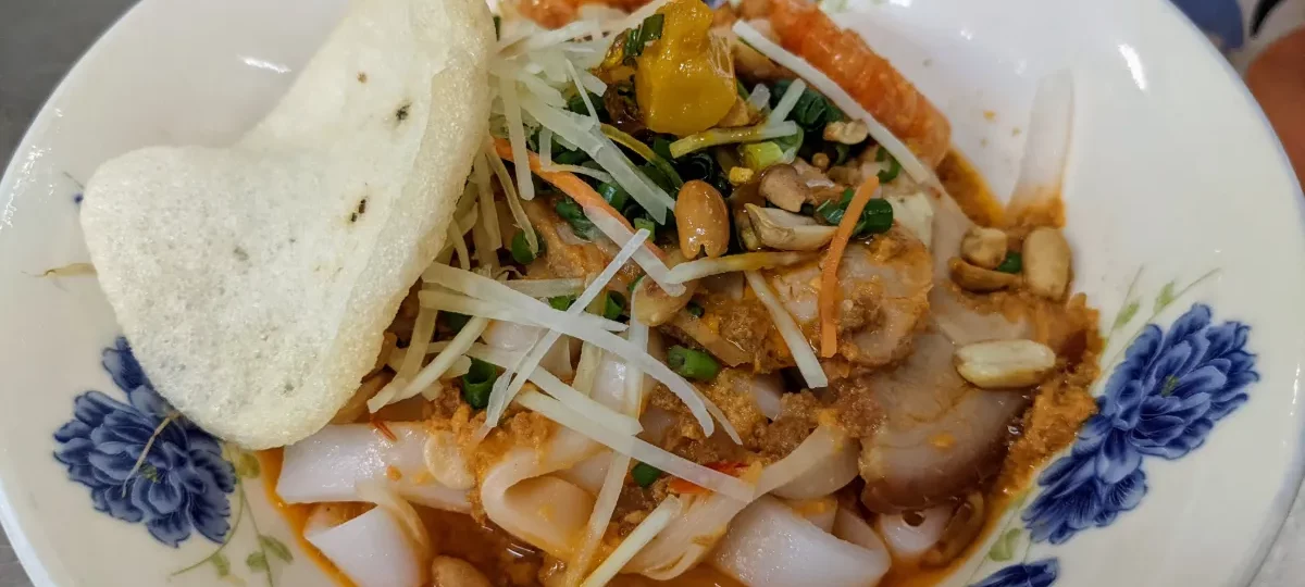 A bowl of mi Quang turmeric noodles with pork, peanuts, herbs and a rice cracker at Mi Quang 1A in Da Nang