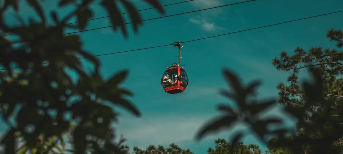 Red Dalat cable car cabin gliding above pine trees against a clear sky on the Robin Hill to Truc Lam line