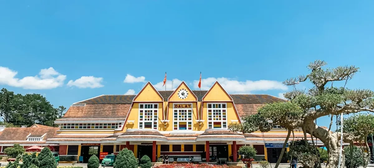 Yellow Art Deco Dalat Railway Station with its three pointed gables and gardens under a bright blue sky