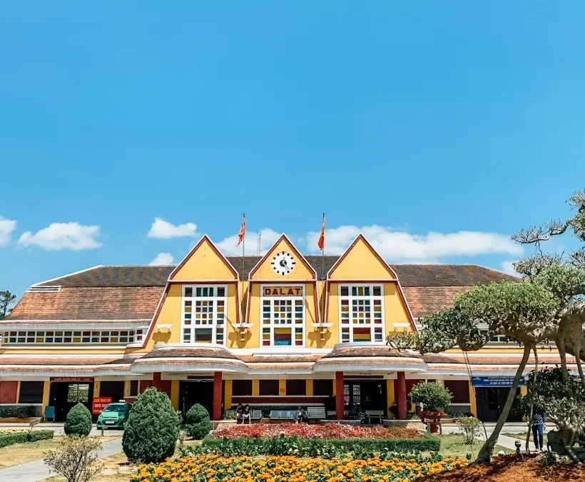 Yellow Art Deco Dalat Railway Station with its three pointed gables and gardens under a bright blue sky