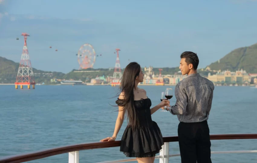 Couple with glasses of wine on deck, with the Nha Trang cable car and Ferris wheel behind