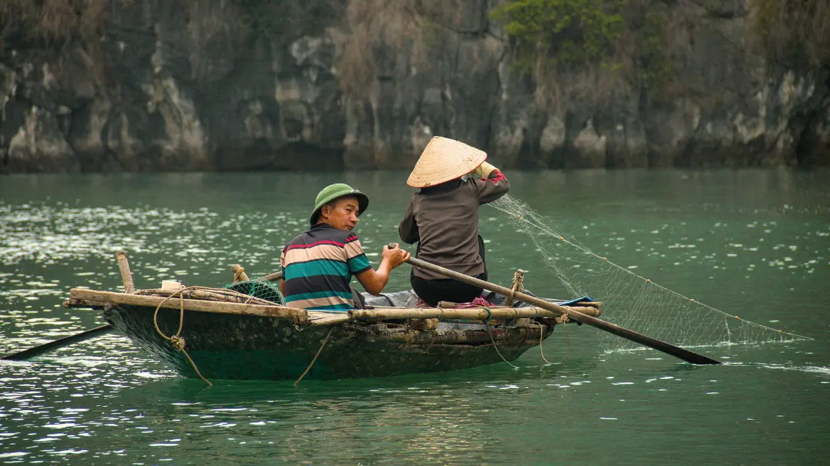 Fishermen Rowing in Bai Tu Long Bay Local fishermen rowing a small boat among limestone cliffs in Bai Tu Long Bay