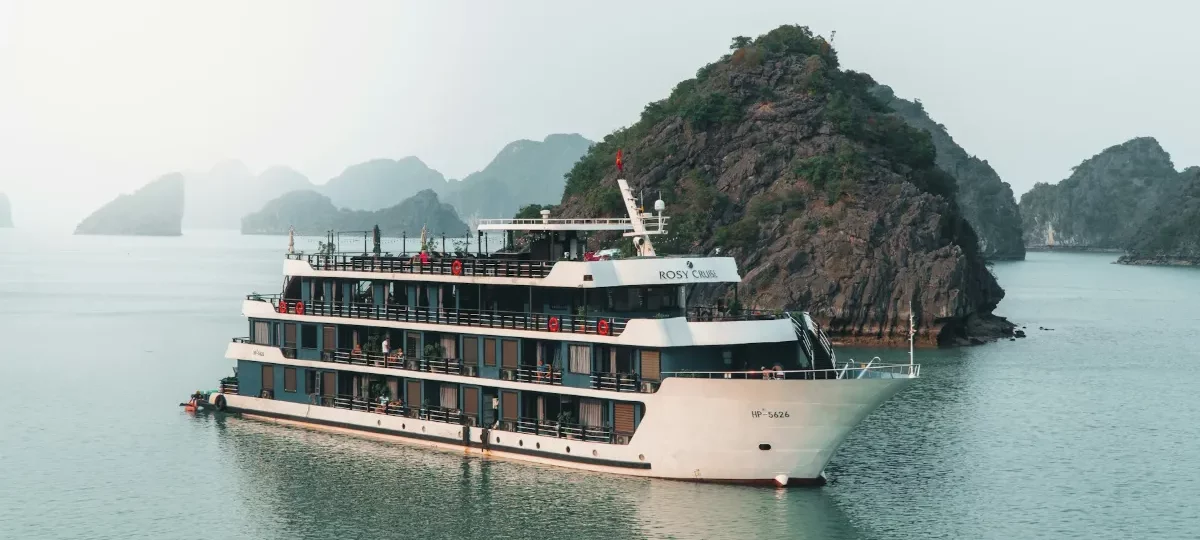 Overnight cruise ship anchored beside limestone karsts in Halong Bay on a calm, misty morning