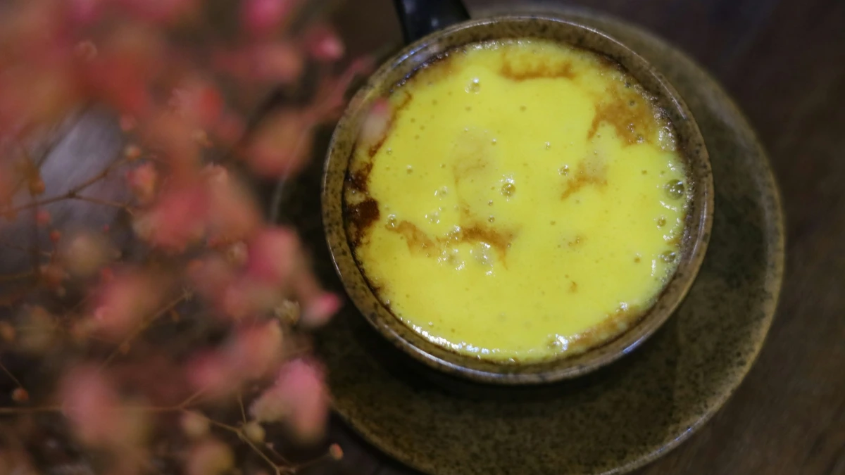 Hanoi Egg Coffee – Close-up of the Egg Foam Close-up of thick yellow egg foam on a cup of egg coffee in Hanoi beside pink flowers