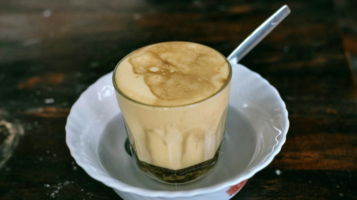 Hanoi Egg Coffee – Served in a Bowl of Hot Water Hot Hanoi egg coffee in a small glass standing in a white bowl of hot water with a spoon