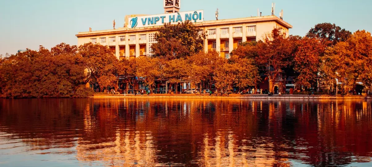 Hoan Kiem Lake at sunset with golden trees and the Hanoi Post Office building reflected in the water