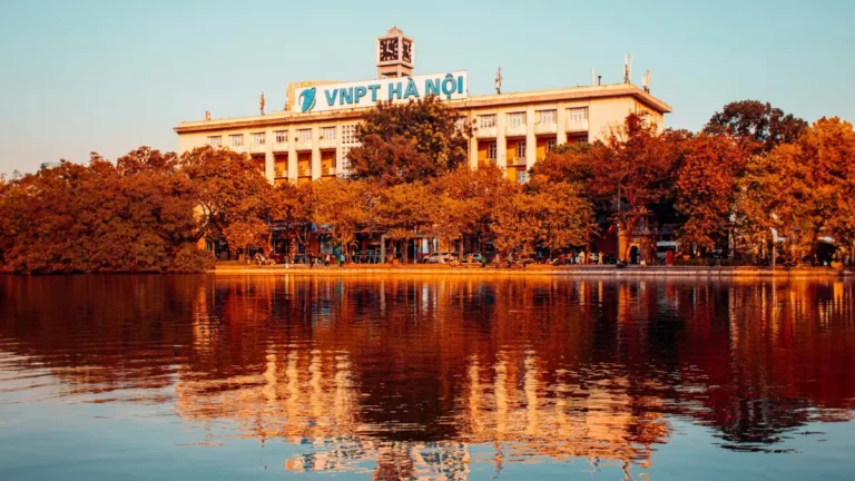 Hoan Kiem Lake at sunset with golden trees and the Hanoi Post Office building reflected in the water