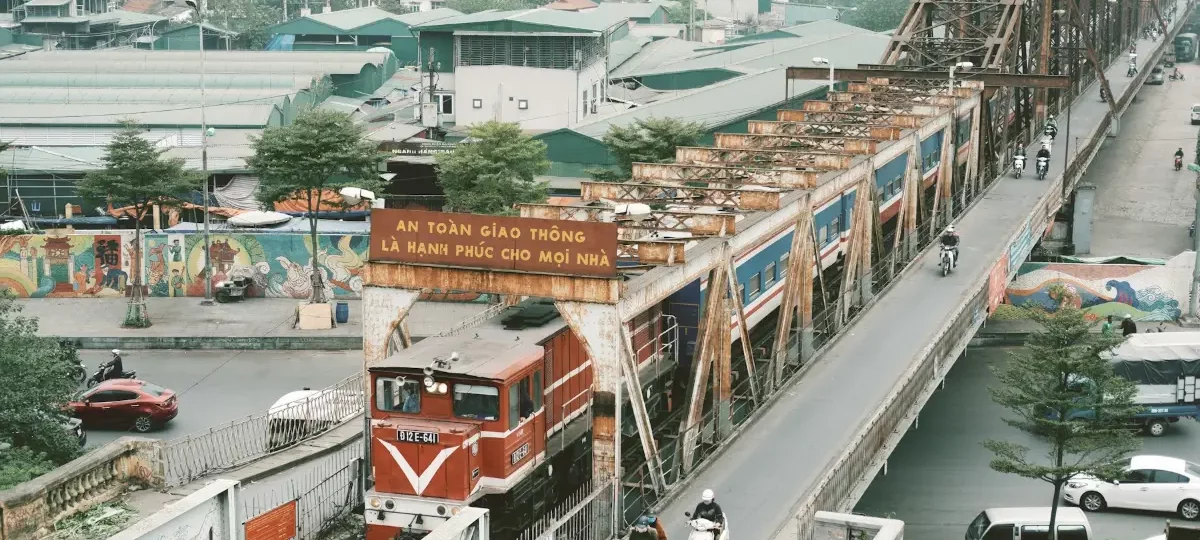 A train crossing Long Bien Bridge in Hanoi while motorbikes ride along the bridge side lane