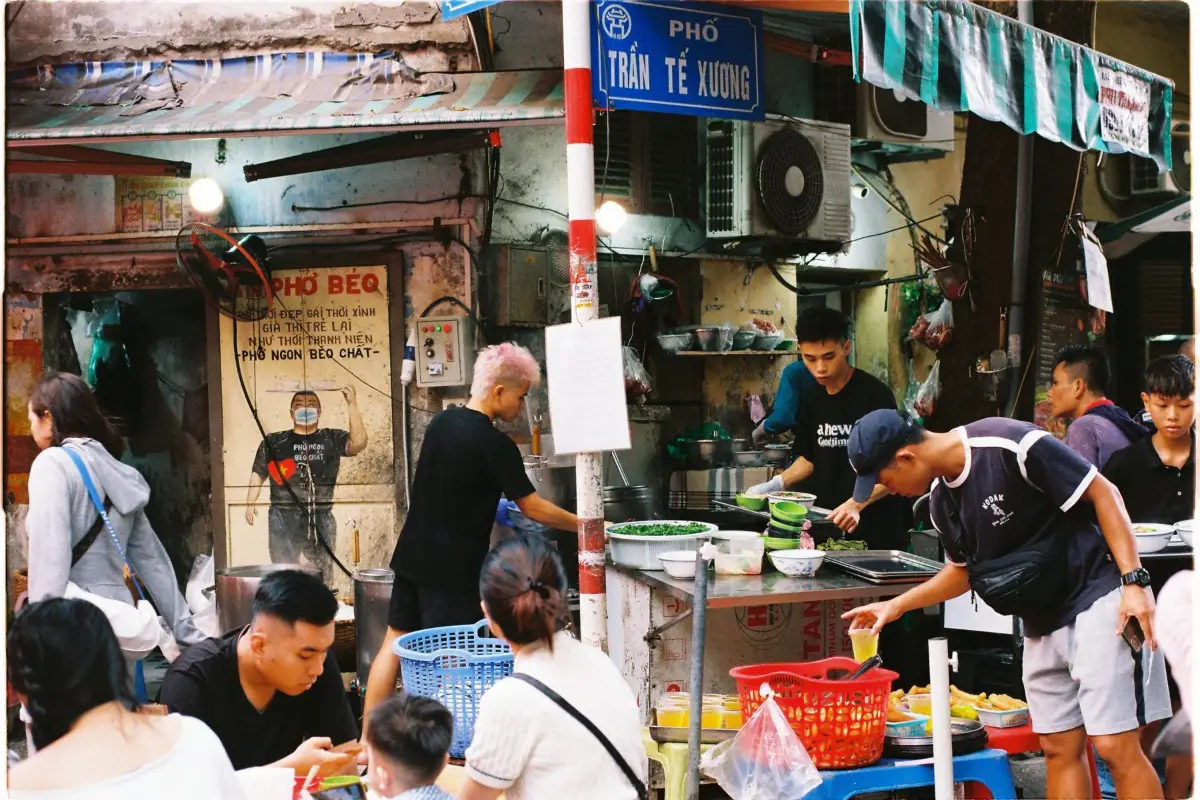 Locals and visitors eating street food on small stools in Hanoi