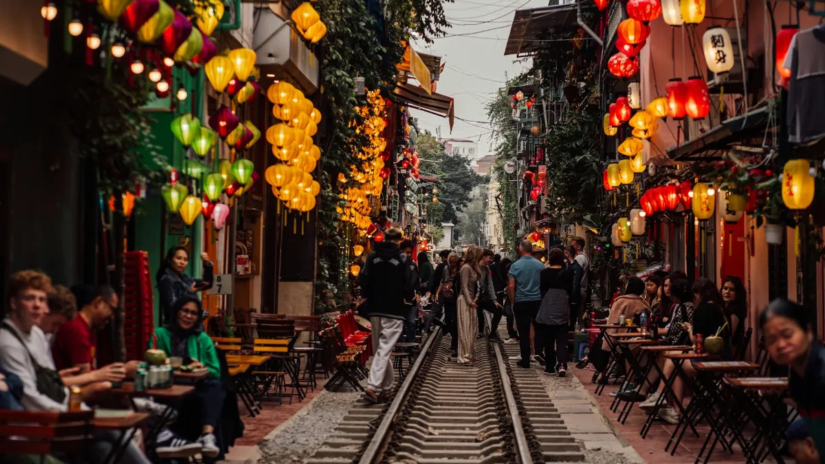 Hanoi Train Street – Cafés Along the Tracks in the Evening Visitors sit at low café tables beside the railway on Hanoi Train Street under coloured lanterns