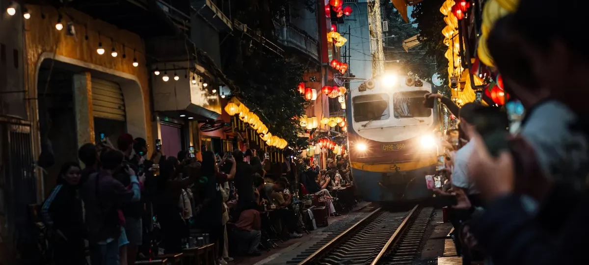 A train passes between crowded trackside cafés on Hanoi Train Street in the Old Quarter at dusk