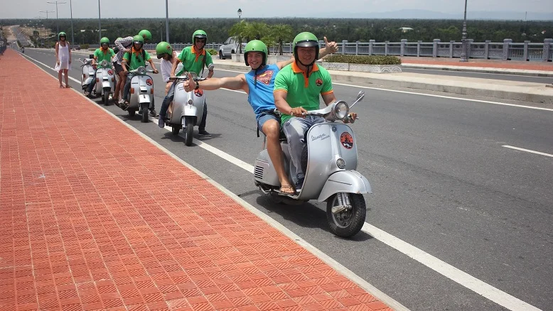 Guest riding pillion on a Vespa along a wide road in central Vietnam