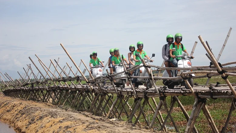 Vespa riders on a bamboo bridge over a river near Hoi An