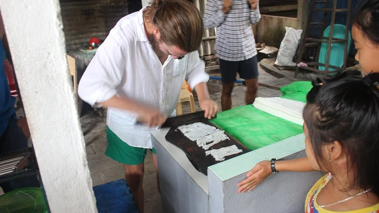 Laying fresh rice paper on bamboo racks to dry at a family workshop near Hoi An