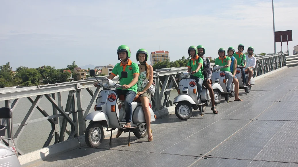Vespa riders crossing a bridge over a river near Hoi An