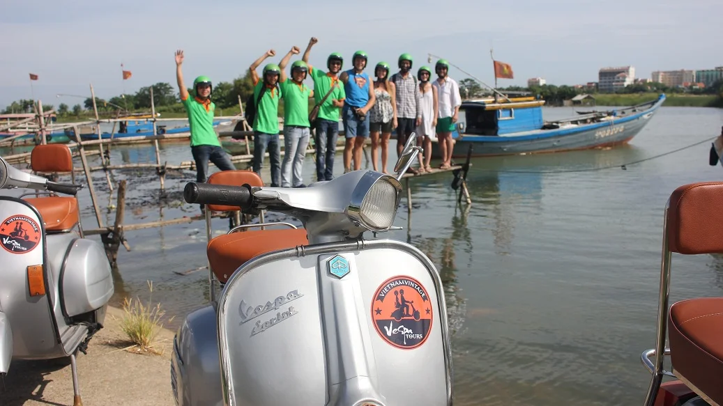 Vespa group by the river with fishing boats near Hoi An