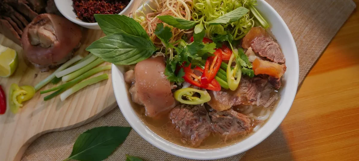 Bowl of bun bo Hue, the spicy lemongrass beef noodle soup that is Hue's signature dish, with herbs and chilli