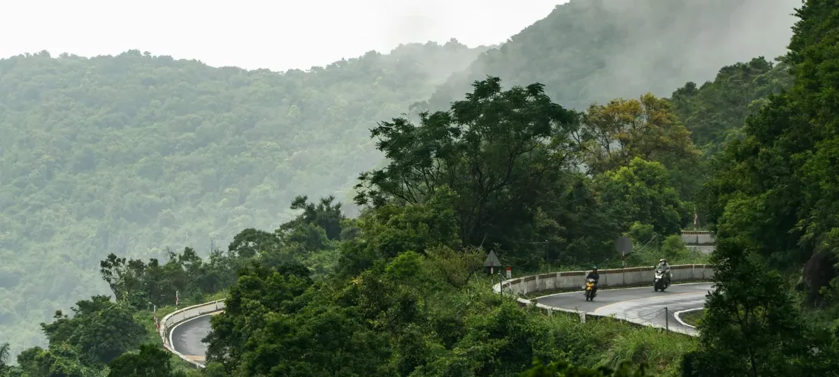 Motorbikes on the winding Hai Van Pass road between Hue and Da Nang, surrounded by green forest