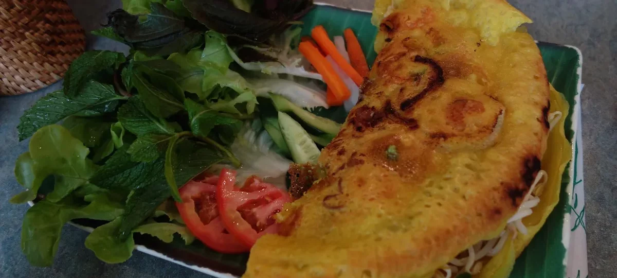 Golden bánh xèo crispy pancake with fresh herbs and lettuce, a favourite dish of Mekong Delta food