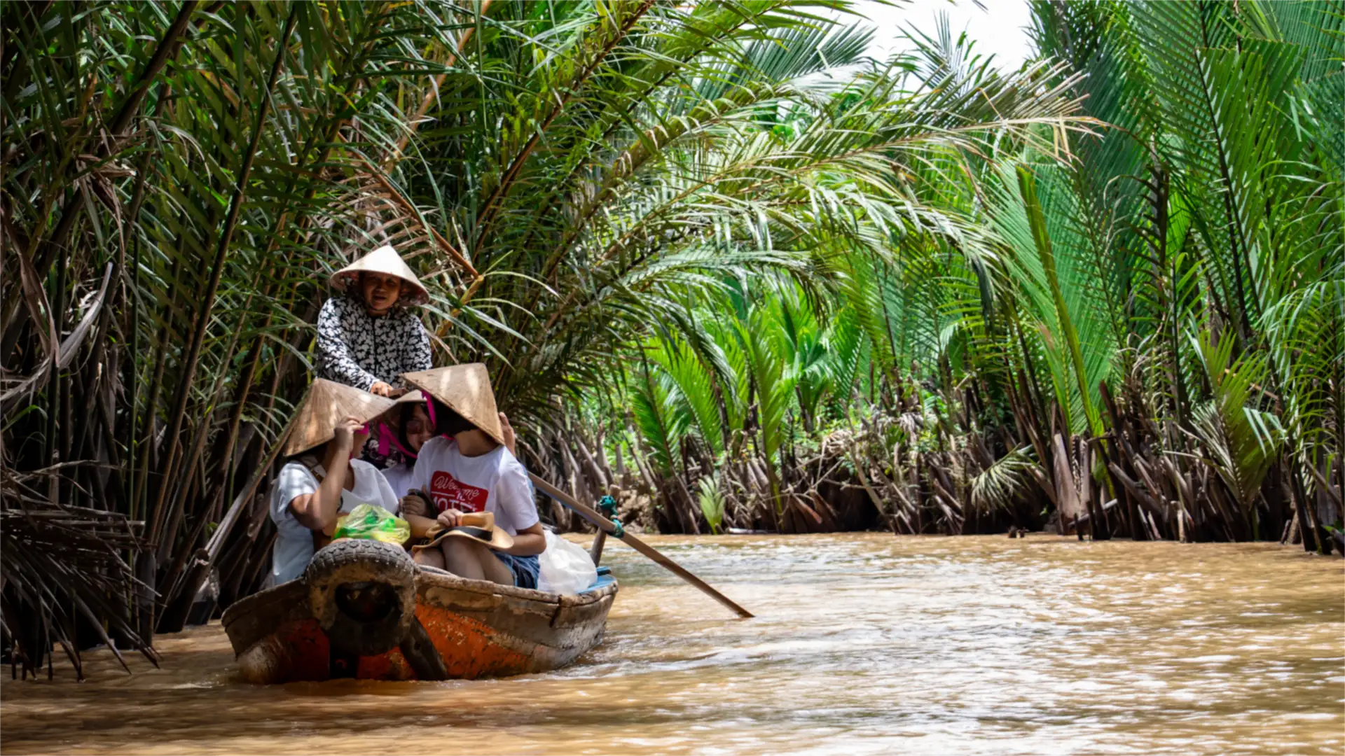 Rowing sampan with conical hats through a water-coconut canal in the Mekong Delta, Vietnam