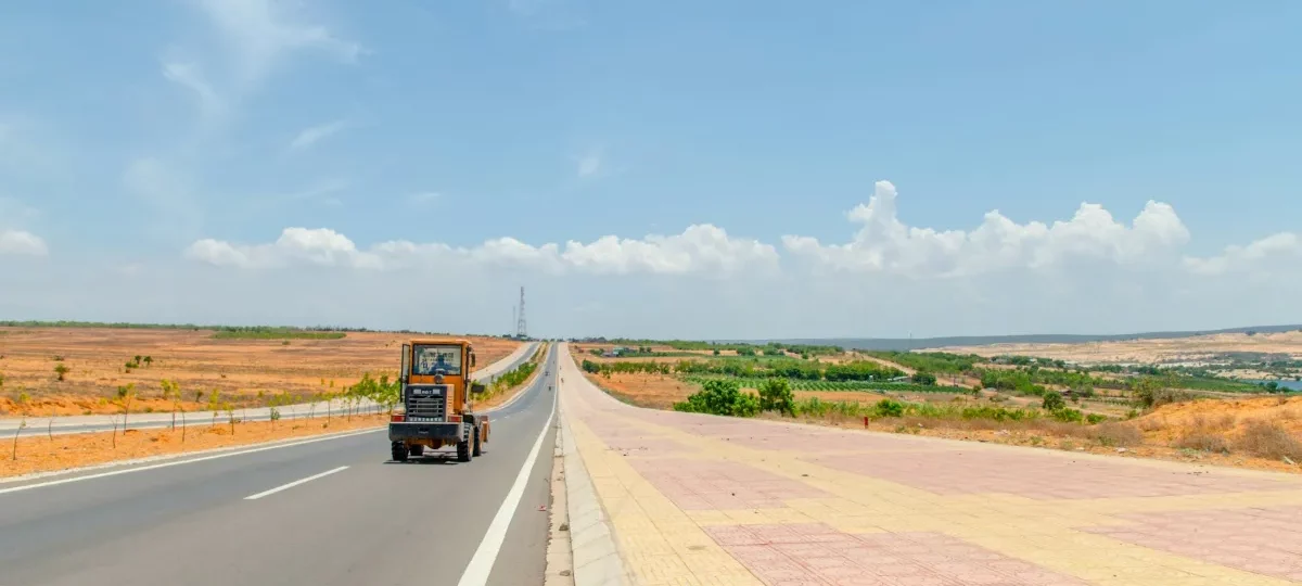 Wide road through the dry red-earth landscape near Mui Ne under a bright blue sky