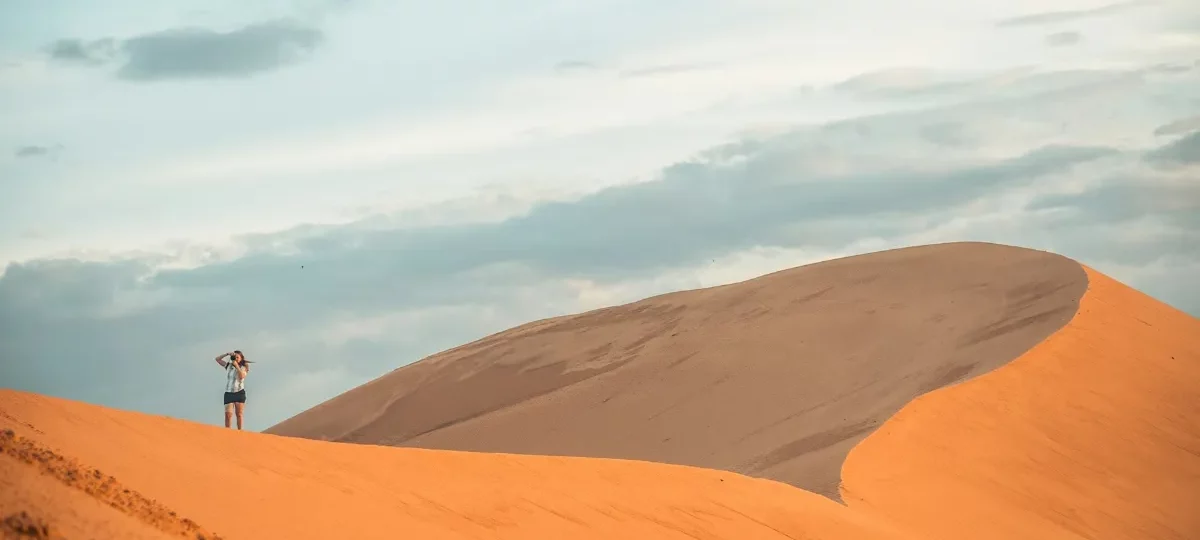 Traveller standing on golden sand dunes in Mui Ne under a soft morning sky