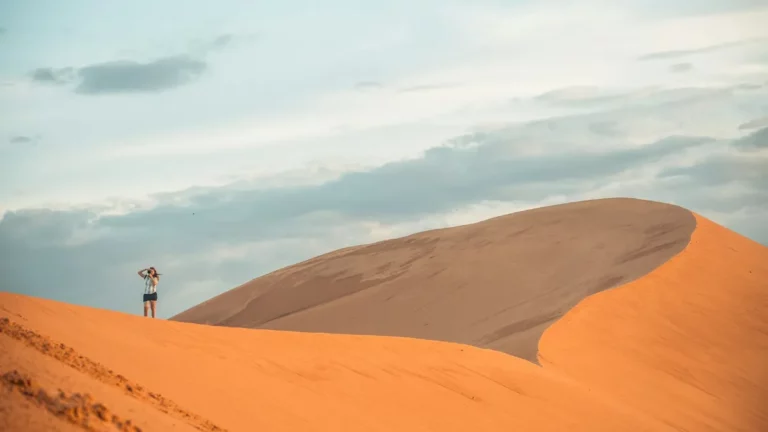 Traveller standing on golden sand dunes in Mui Ne under a soft morning sky