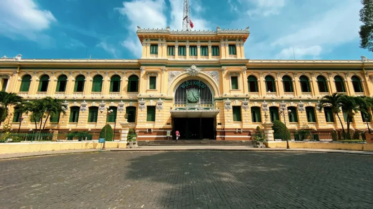 Yellow French colonial facade of the Saigon Central Post Office under a blue sky in Ho Chi Minh City