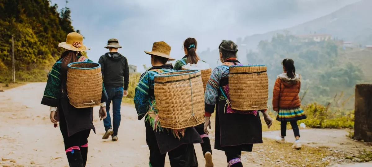 Hmong women with woven baskets leading trekkers along a mountain trail near Sapa