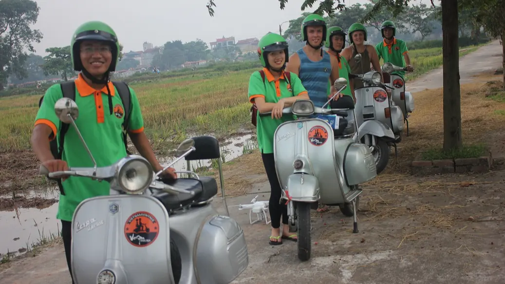 Vespa guide and guests by a rice field